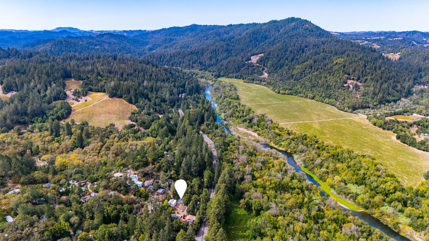 Aerial view of homes near a winding river and forested hills, with a location pin marking the property.