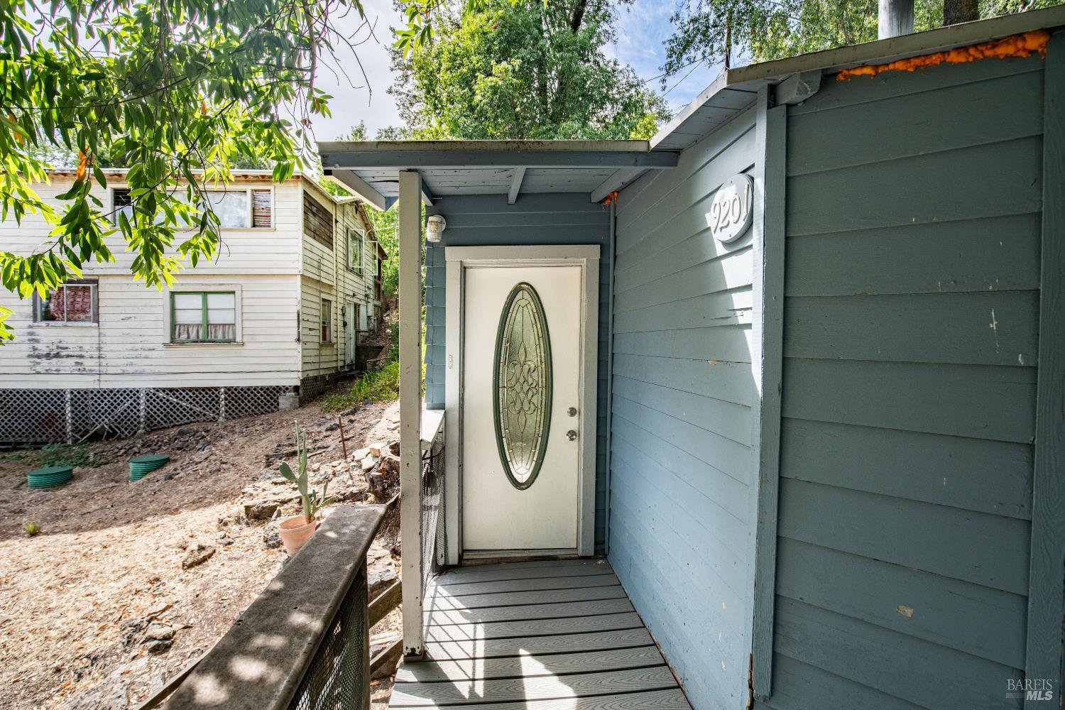 Covered entry of a blue-sided home with a white decorative glass door and sloped yard.