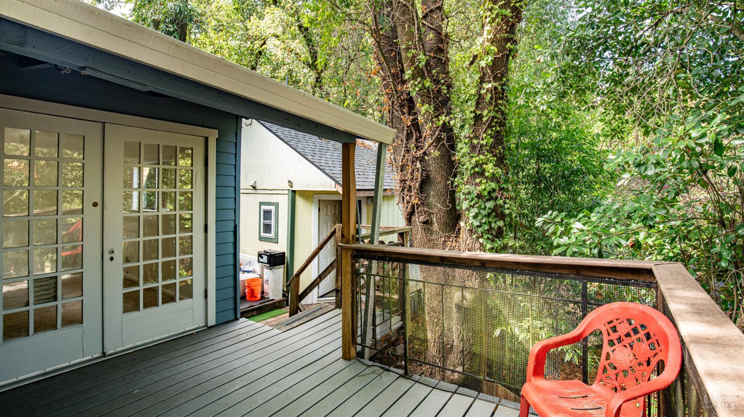 Wooded home deck with gray plank flooring, glass-paneled doors, and a red chair.