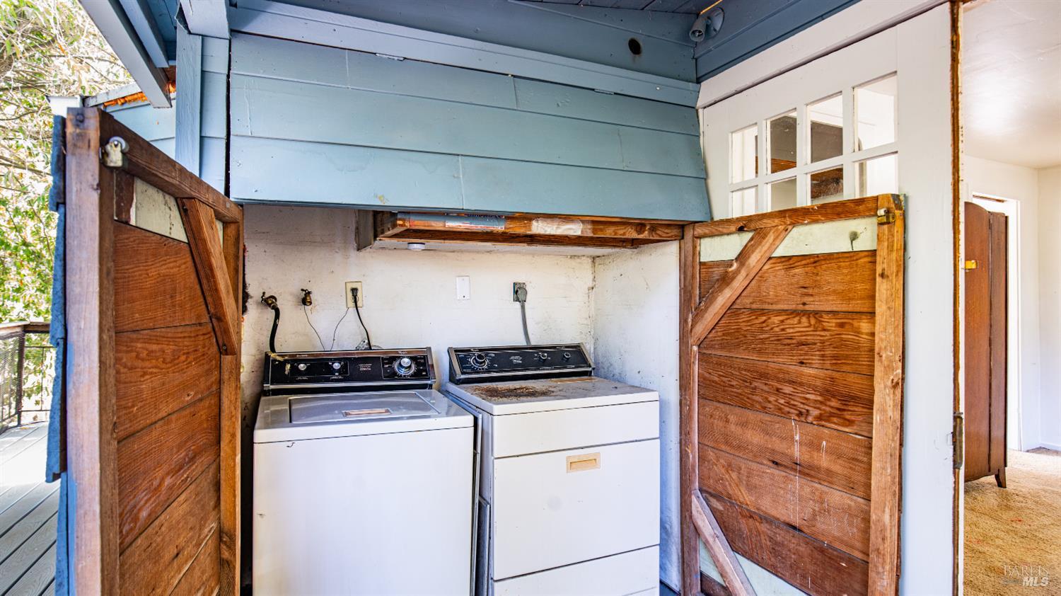 Exterior laundry area with a washer and dryer behind open wooden doors.