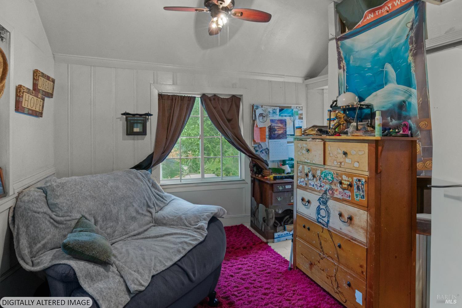 Bedroom with a gray-covered sofa, sticker-covered wooden dresser, magenta rug, and dolphin poster.