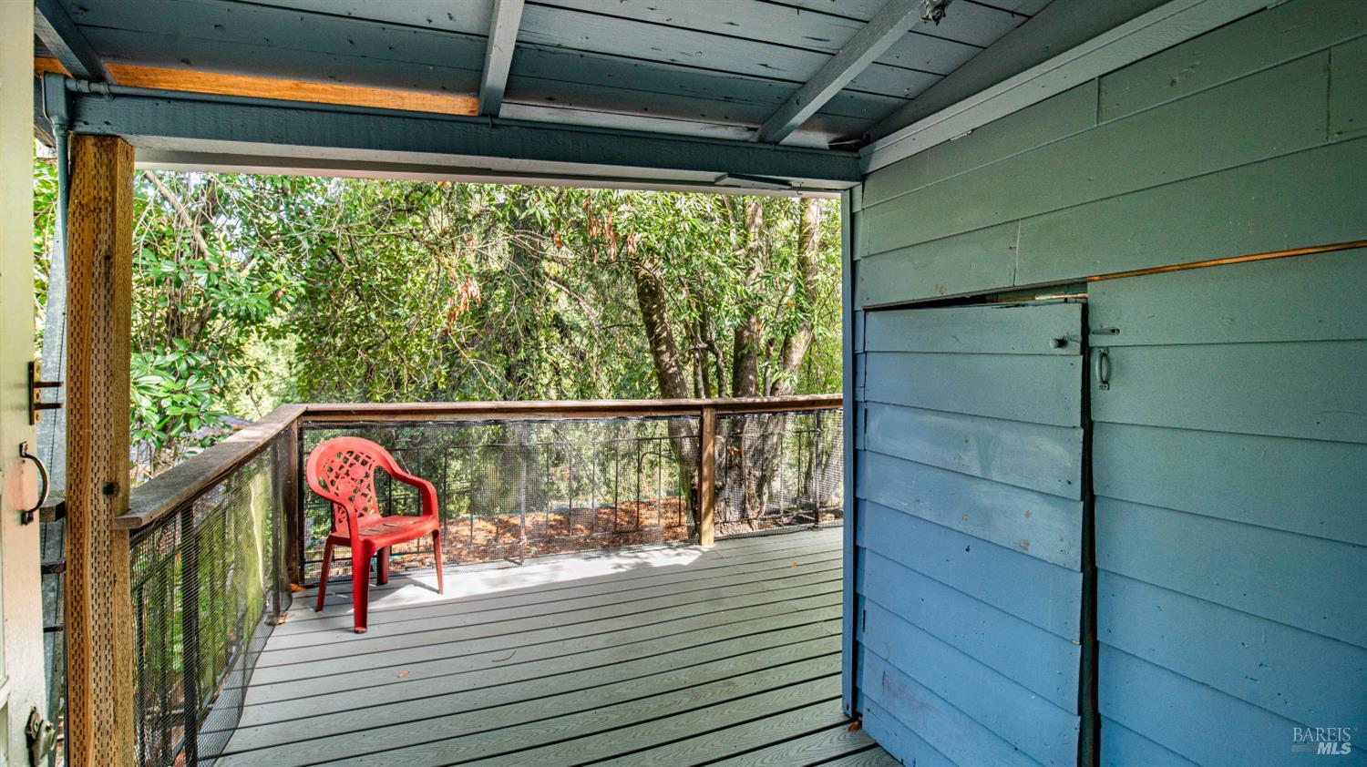 Covered blue deck overlooking trees, with a red chair beside the screened railing.