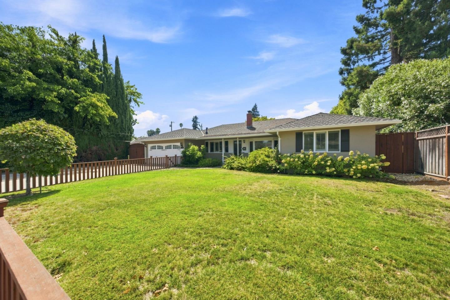 Single-story house behind a broad green lawn, with an attached garage and flowering shrubs.