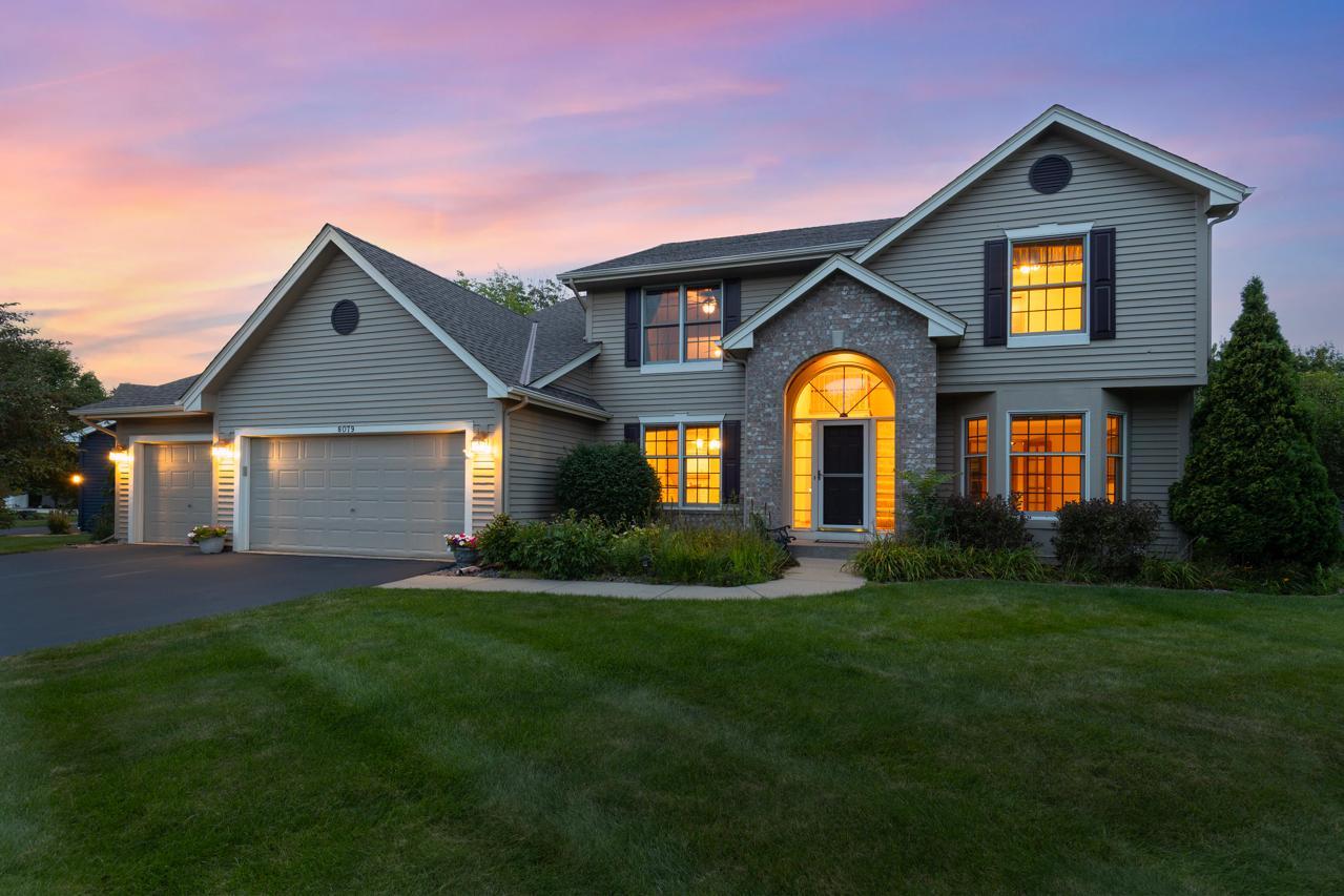Two-story gray home with a stone entry and glowing windows at dusk.