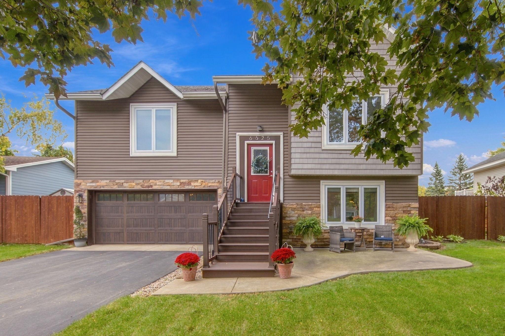 Split-level home with brown siding, stone accents, a red entry door, and a double garage.