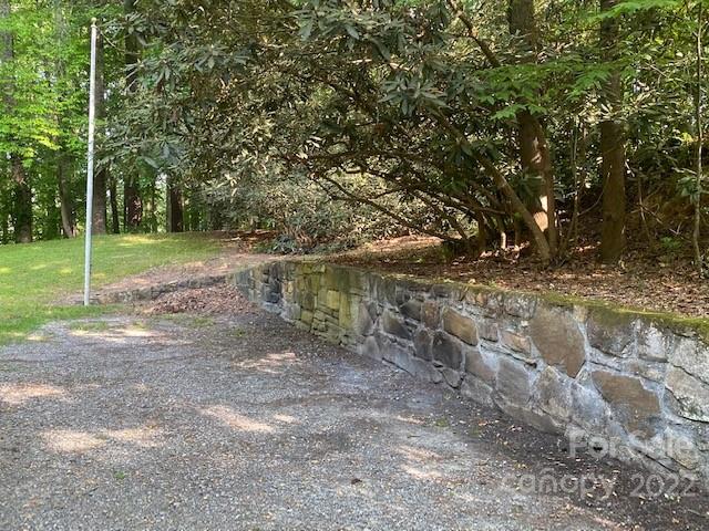 Gravel driveway bordered by a stone retaining wall and shaded woodland.
