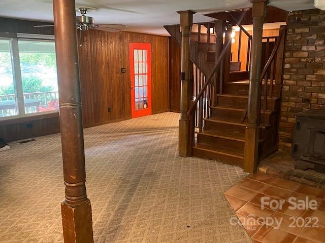 Wood-paneled room with patterned carpet, red door, staircase, stone fireplace, and large windows.