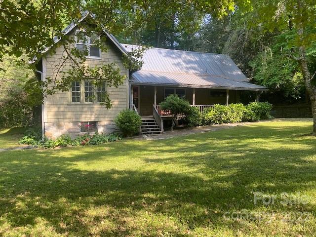 House with a metal roof and covered porch set among trees beside a broad lawn.