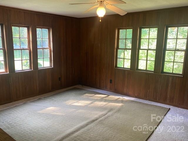 Unfurnished wood-paneled room with a ceiling fan and multiple windows overlooking greenery.