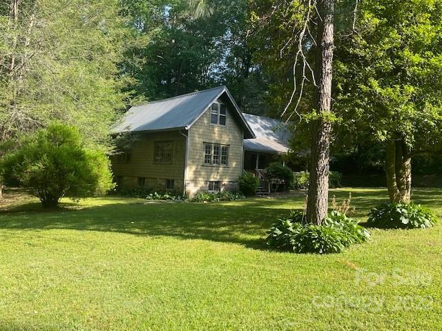 Gray cottage with a metal roof and covered porch surrounded by trees on a sunny lawn.