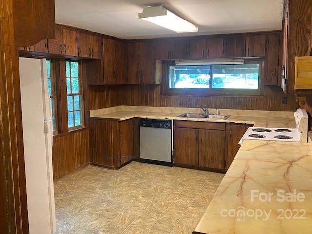 Kitchen with dark wood cabinets, patterned countertops, a window above the sink, dishwasher, and electric range.