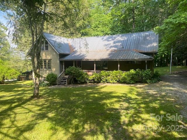 House with a metal roof and covered porch, surrounded by mature trees and lawn.