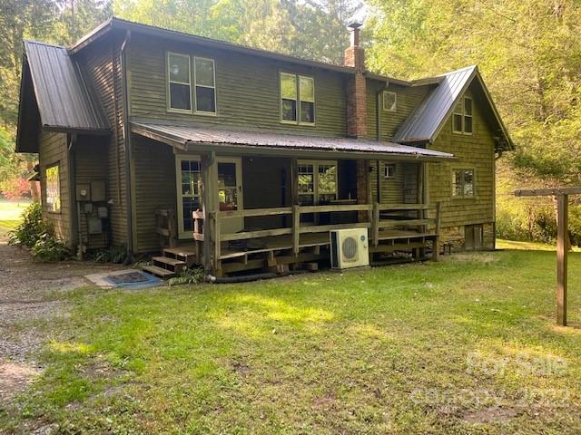Two-story green-sided house with a covered porch and wooded yard.