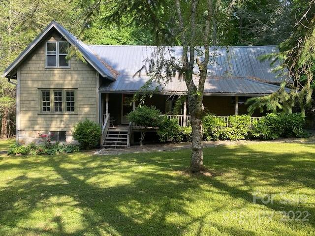 Gray-green house with a metal roof and covered porch, set among mature trees.