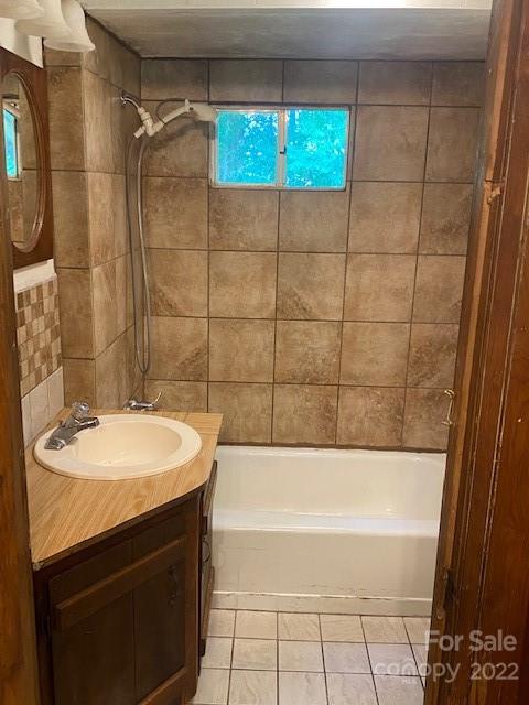 Bathroom with a tiled tub and shower, wood vanity, and small high window.