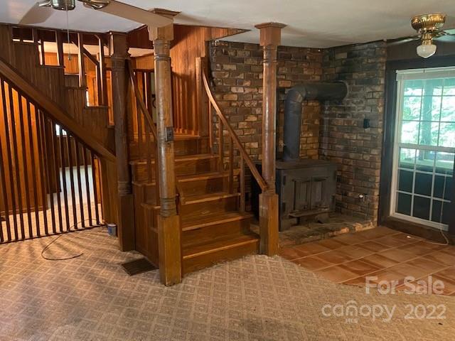 Interior with a wooden staircase, brick walls, a freestanding wood stove, and a large window.