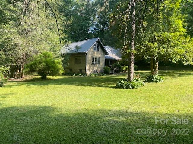 Gray cottage with a steep metal roof and covered porch in a tree-lined lawn.