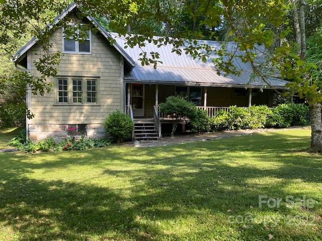 House with a metal roof, covered porch, and tree-shaded front lawn.