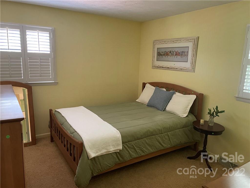 Bedroom with a wooden bed, green bedding, plantation shutters, and beige carpet.
