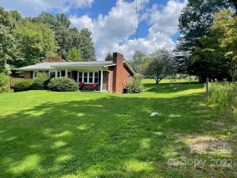 Ranch house with a brick chimney, large windows, and a broad lawn shaded by mature trees.
