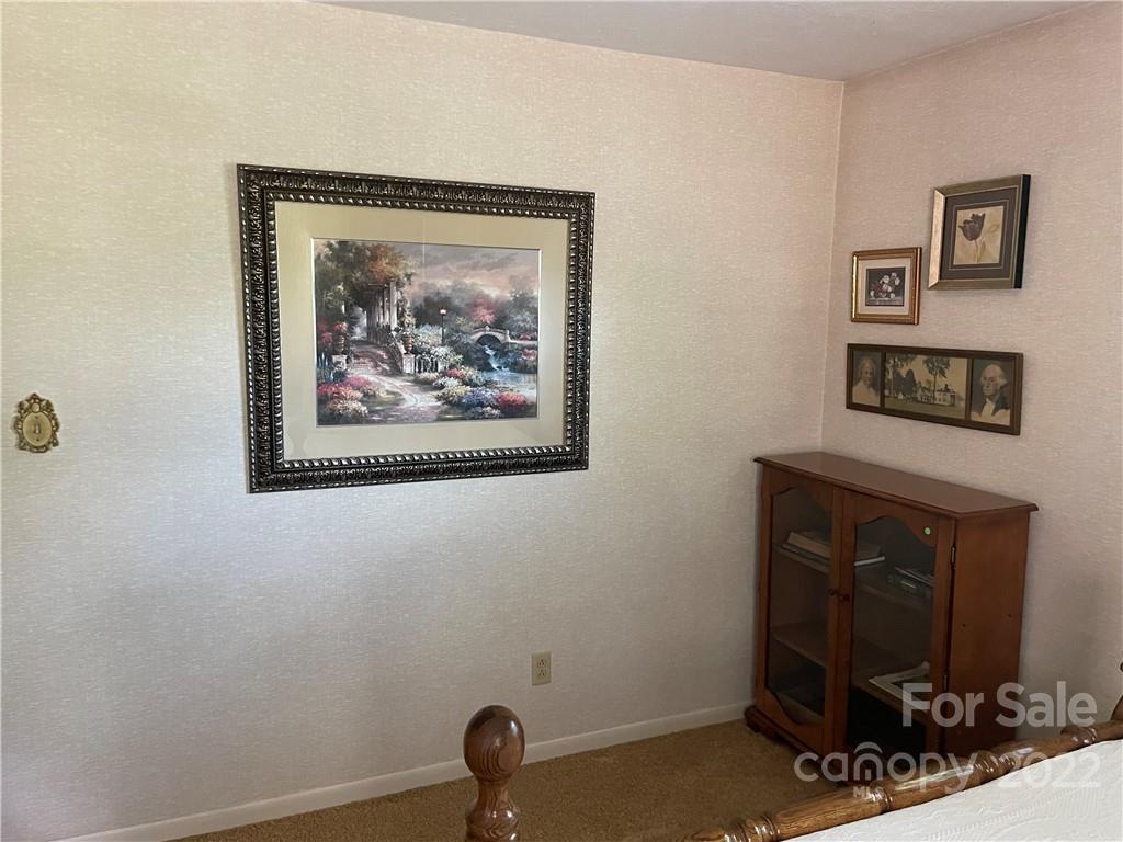 Bedroom with framed artwork, beige carpet, and a wooden glass-front cabinet.