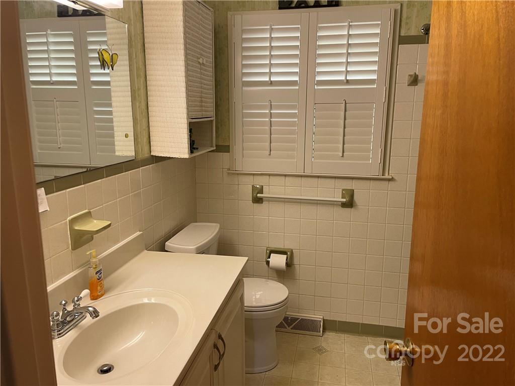 Bathroom with a white vanity and sink, tiled walls, and a window with plantation shutters.
