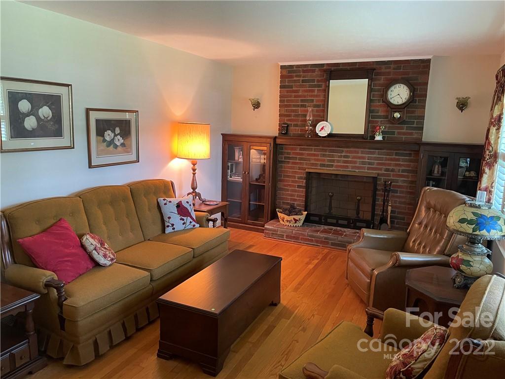 Furnished living room with a brick fireplace, green sofa, leather chairs, and hardwood floors.