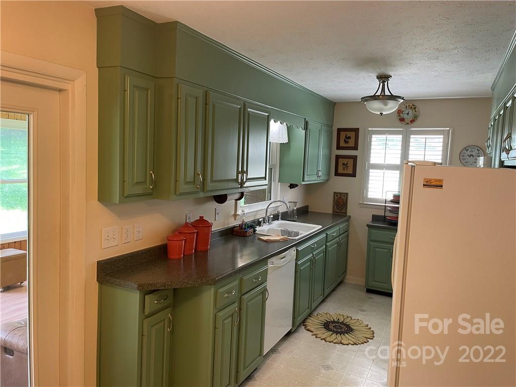 Kitchen with sage-green cabinets, dark countertops, and a sun-shaped rug on the tile floor.