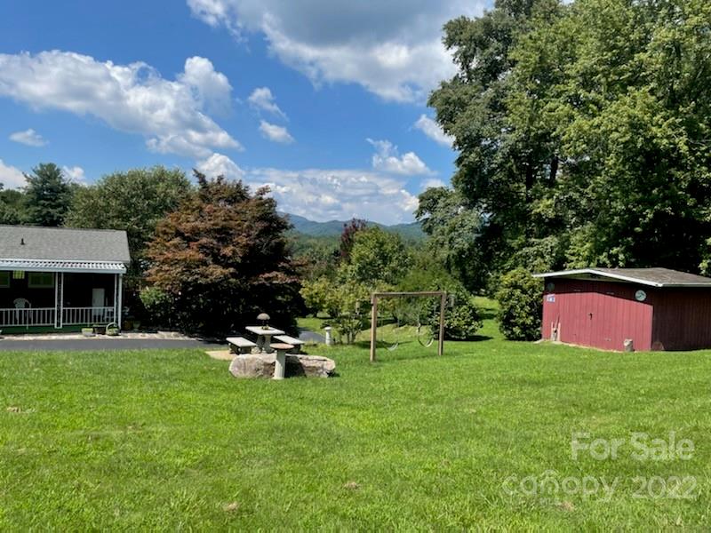 Broad lawn with a picnic table and swing frame, flanked by a house and red shed with mountains beyond.