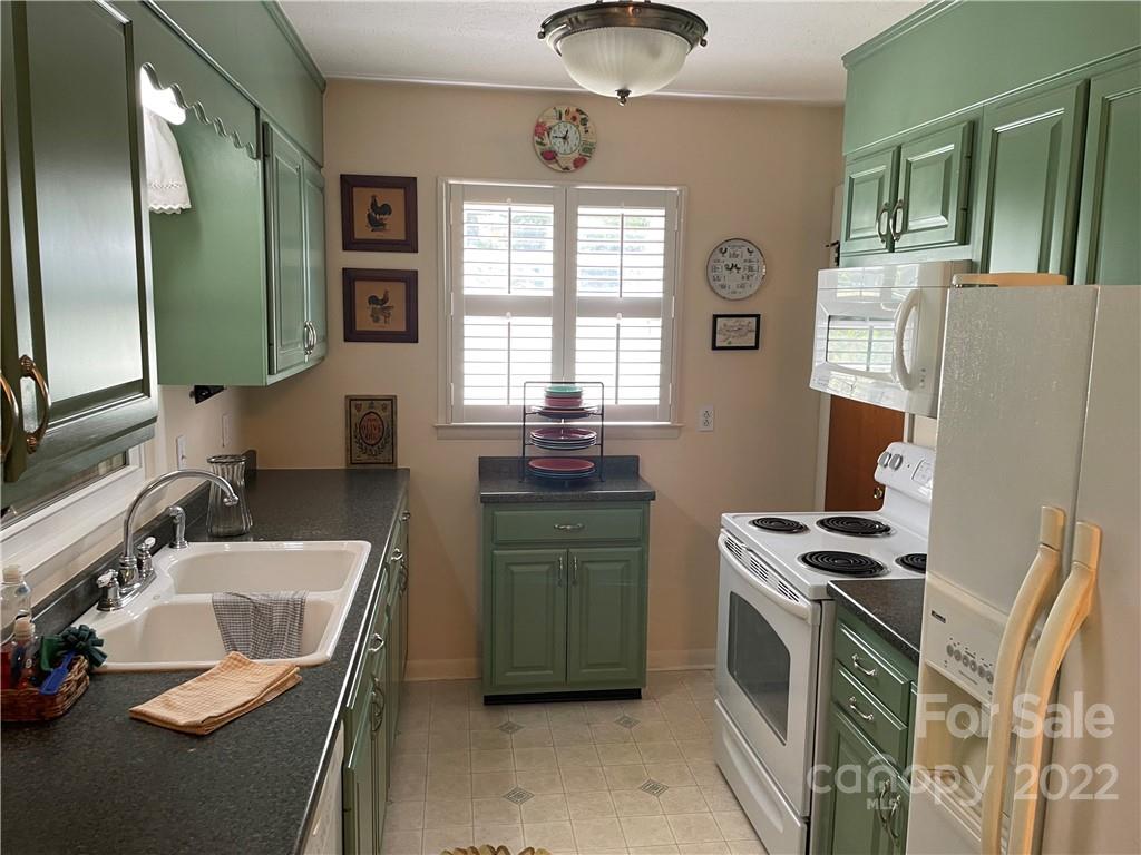 Kitchen with green cabinets, dark countertops, shuttered windows, and white appliances.