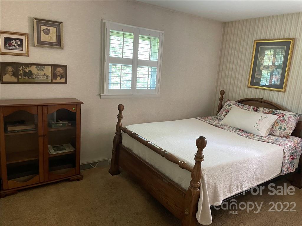Bedroom with a dark wooden four-poster bed, floral pillows, and a shuttered window.