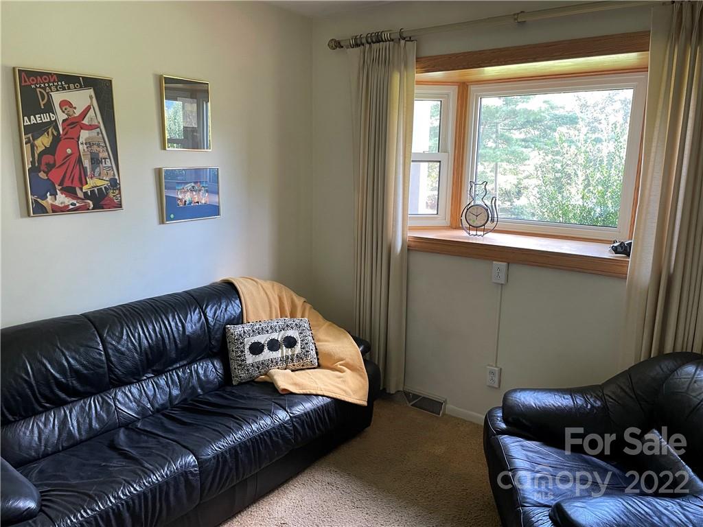 Living room with black leather sofas and a large wood-trimmed window overlooking trees.