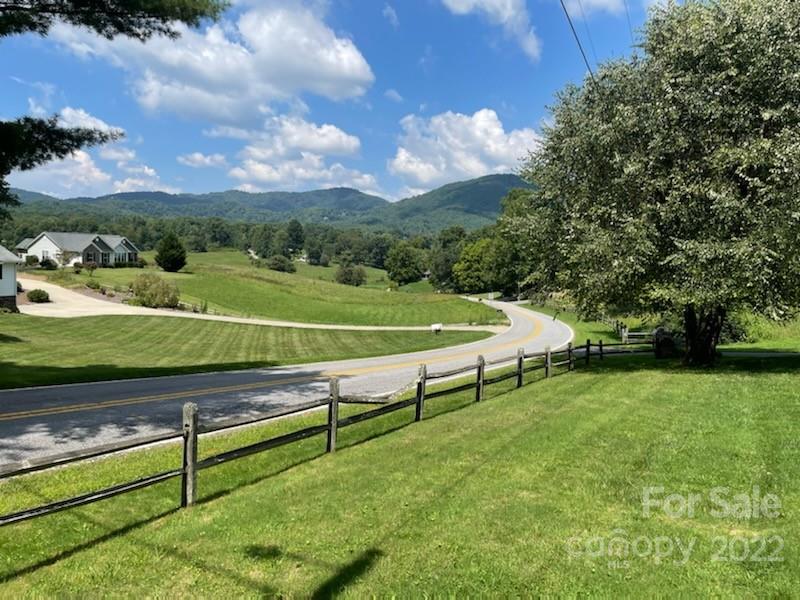 Lawn and split-rail fence overlook a curving road and distant mountain ridges.