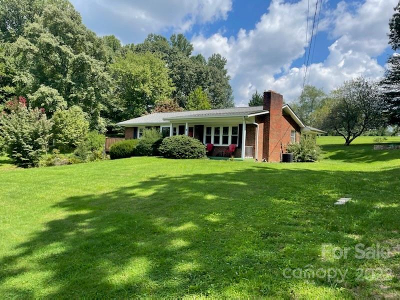 Ranch-style home with a covered porch and brick chimney beyond a broad green lawn.