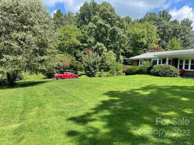Single-story home beyond a broad lawn, with mature trees and a red pickup truck.