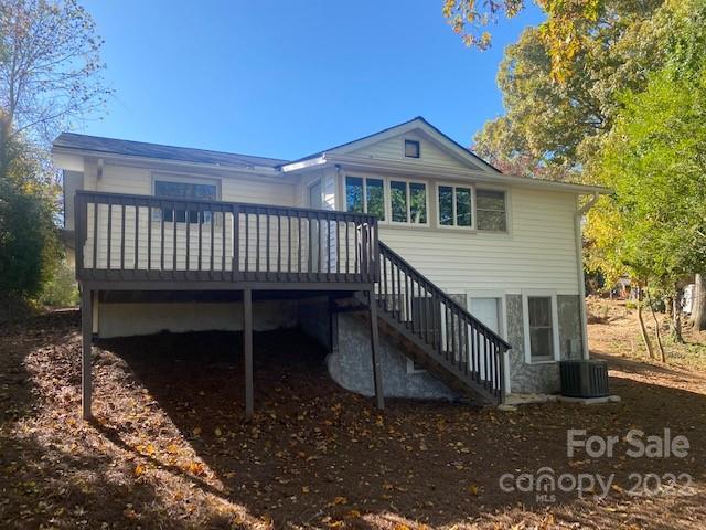 White house with a raised dark deck and stairs, surrounded by autumn trees.