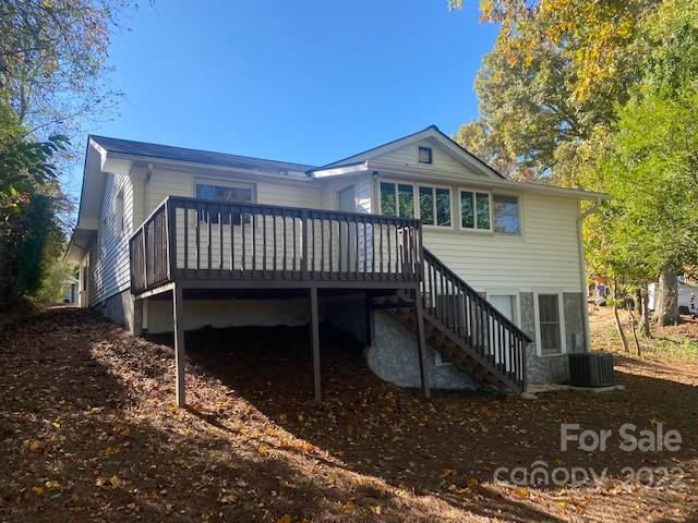 Light-colored house with a raised deck and long staircase among autumn trees.