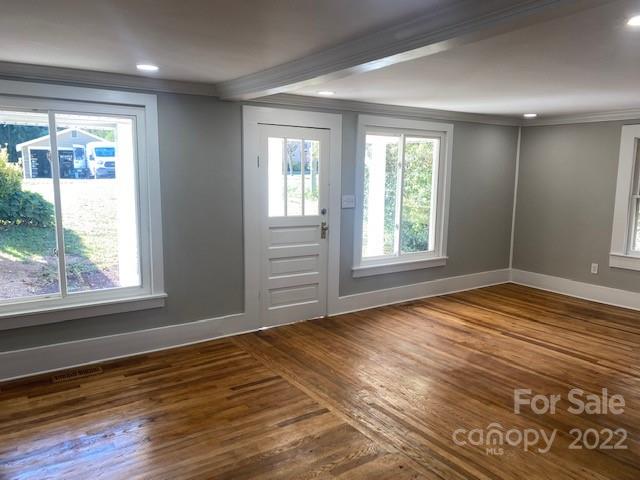 Unfurnished room with hardwood floors, gray walls, and a white entry door.