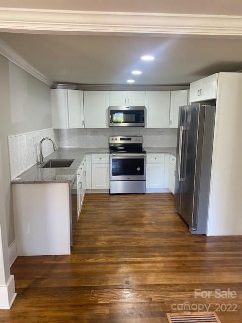 White-cabinet kitchen with stainless steel appliances, granite counters, and hardwood flooring.
