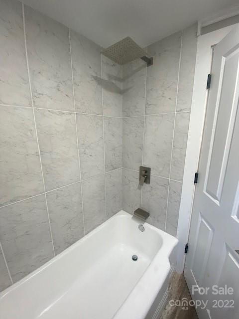 Bathroom with a white bathtub, gray tile surround, and overhead showerhead.
