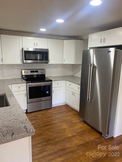 Kitchen with white cabinets, stainless steel appliances, speckled stone counters, and warm wood flooring.