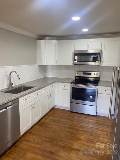 Kitchen with white cabinets, gray countertops, stainless-steel appliances, and warm wood flooring.