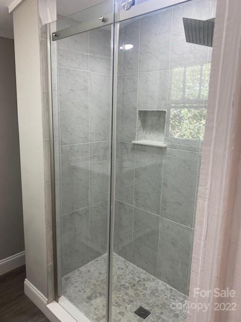 Walk-in shower with clear glass doors, gray tile walls, a built-in shelf, and pebble-tile flooring.