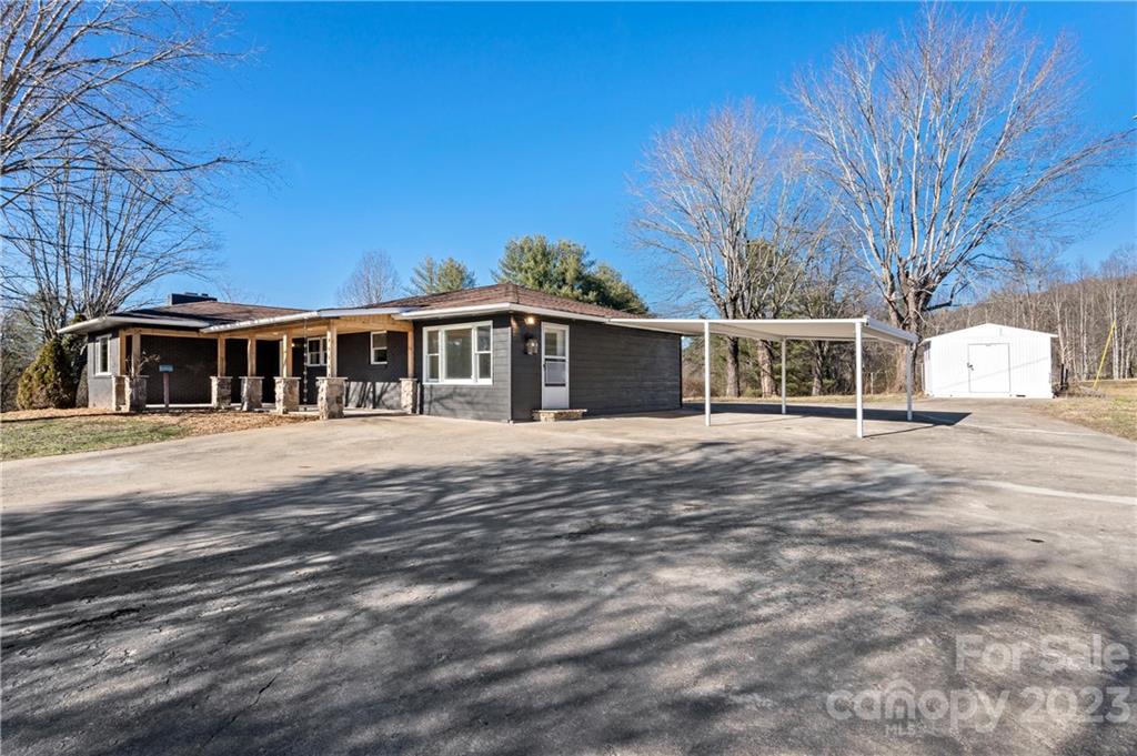 Single-story home with a covered porch, metal carport, and detached white outbuilding.