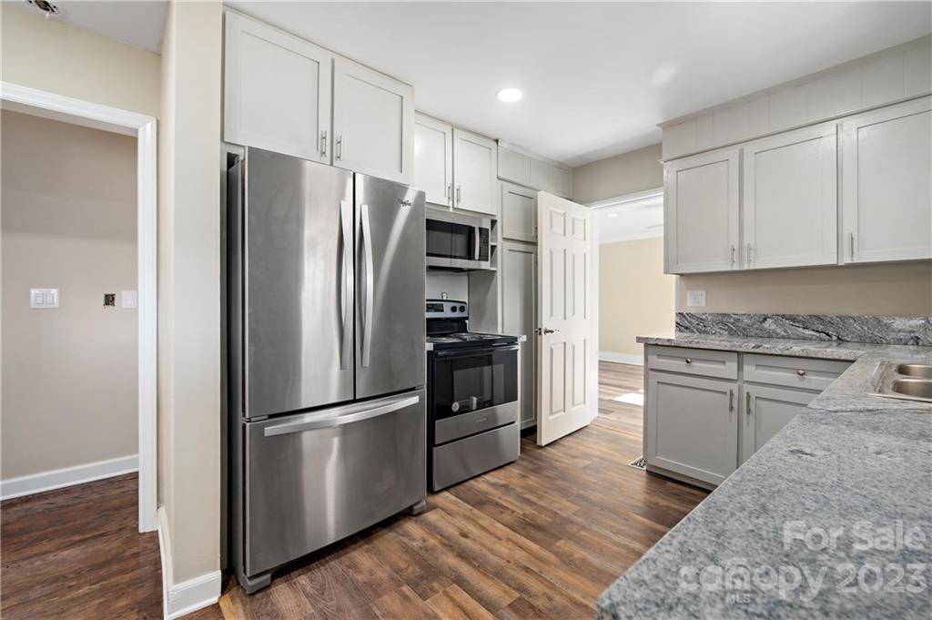 Kitchen with white cabinets, gray stone counters, stainless steel appliances, and wood-look flooring.