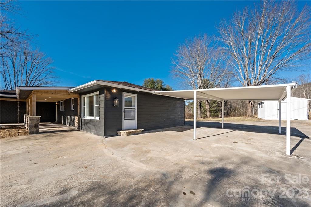 Single-story dark-sided home with a white metal carport and broad concrete driveway.