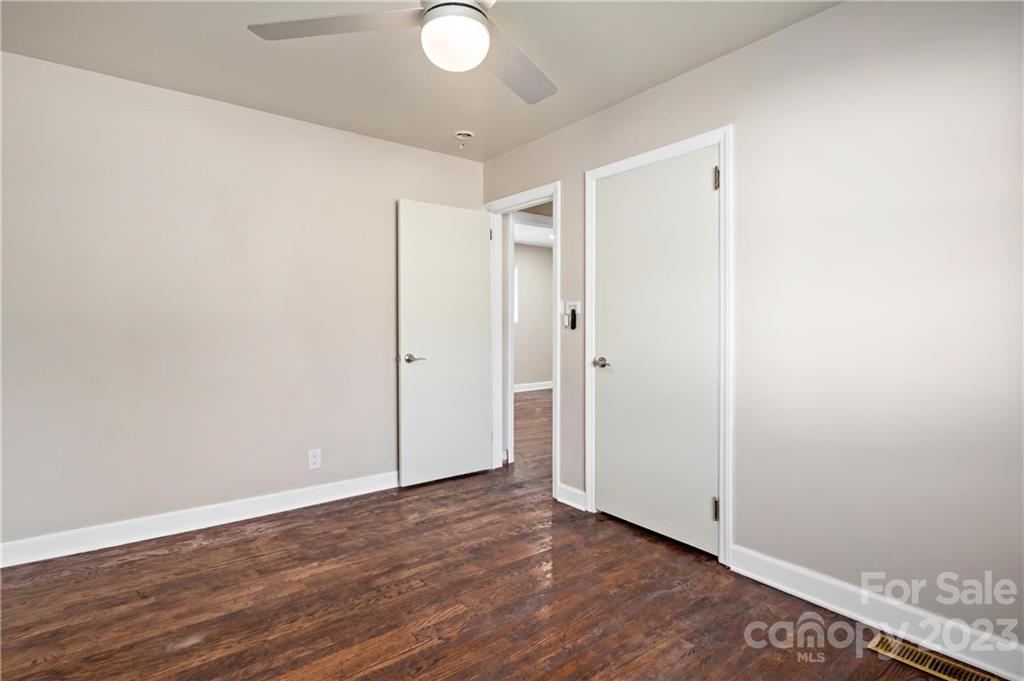 Empty room with dark wood floors, a ceiling fan, and two open white doors.
