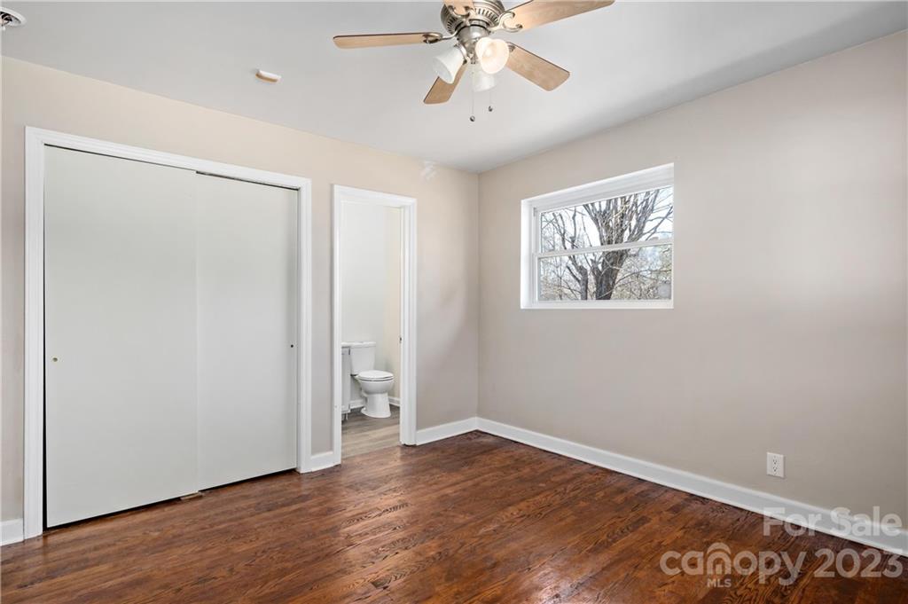 Empty bedroom with hardwood floors, a ceiling fan, and a bathroom doorway.