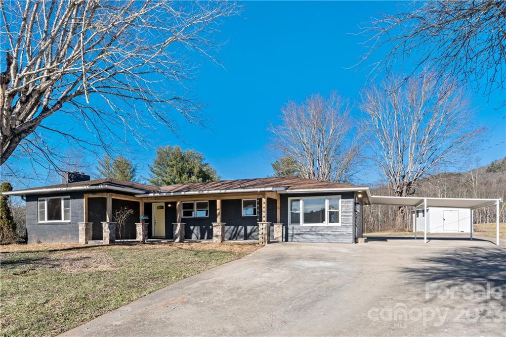 Single-story blue-gray home with a covered porch, wide driveway, and white carport.