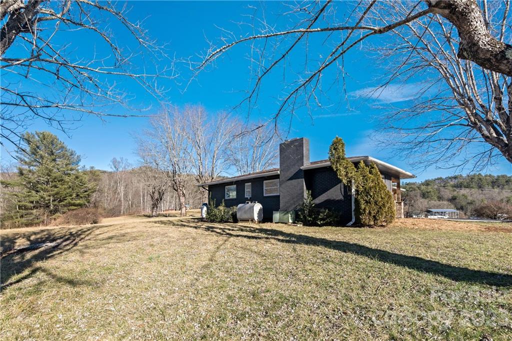Dark-sided house with a tall chimney on a broad grassy lot beneath a clear blue sky.